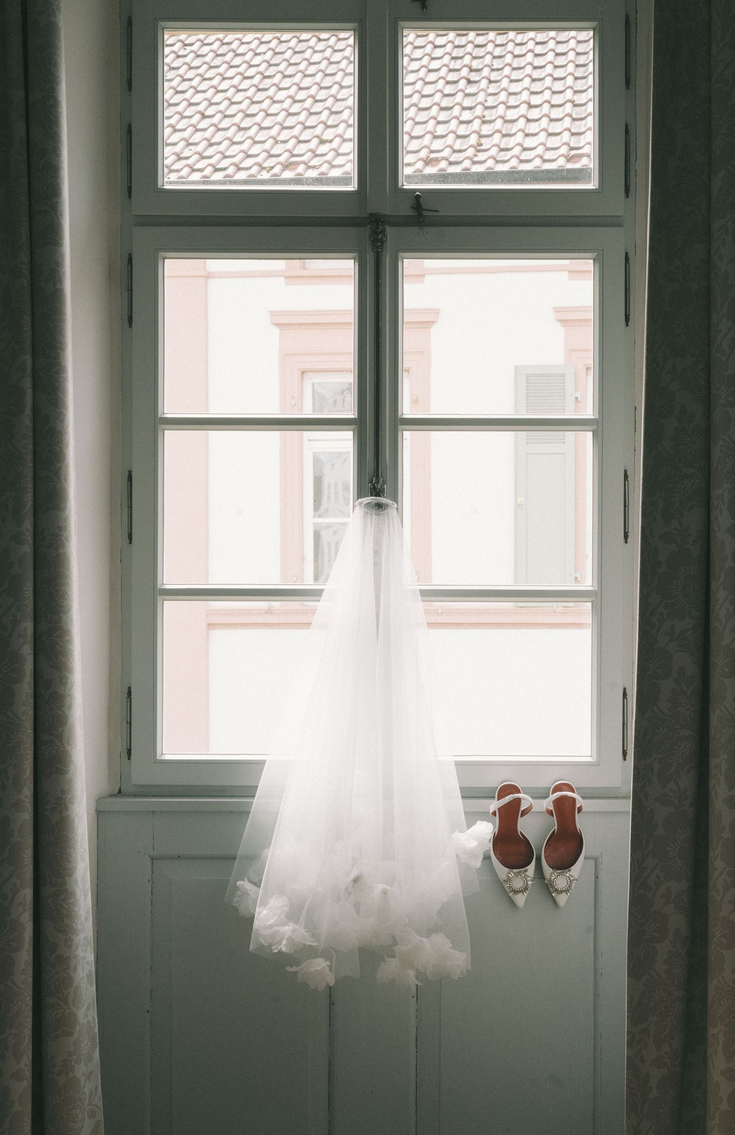 Ethereal white dresses hanging by windows creating a dreamy silhouette against natural light.