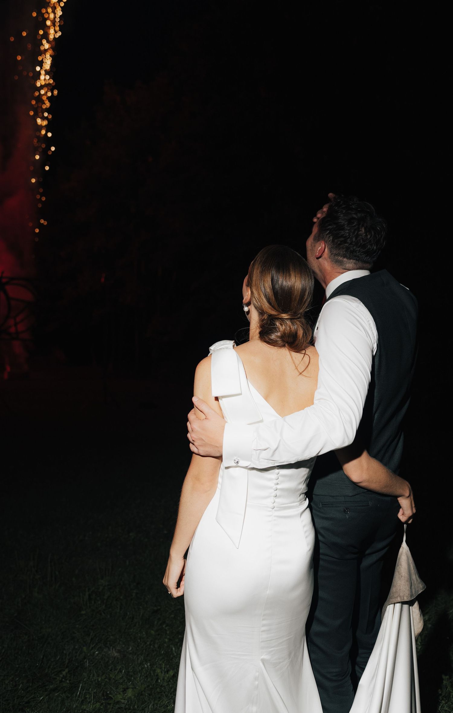 Couple in formal attire watching fireworks display together at nighttime event.