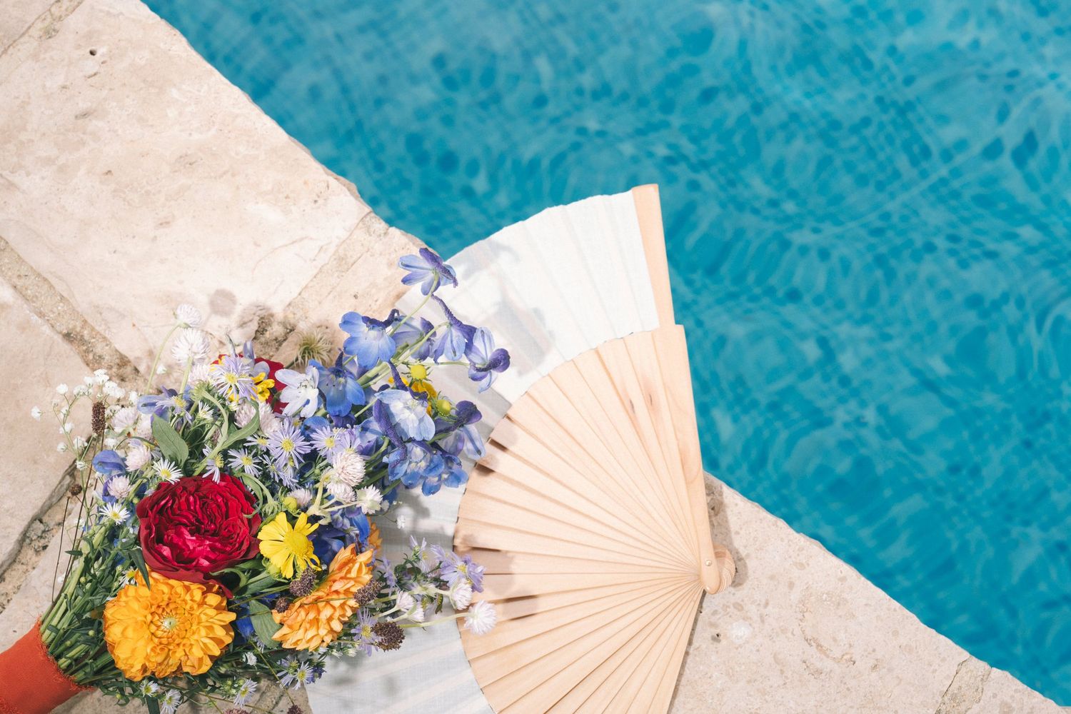 Decorative fan and colorful floral arrangement beside turquoise pool water.