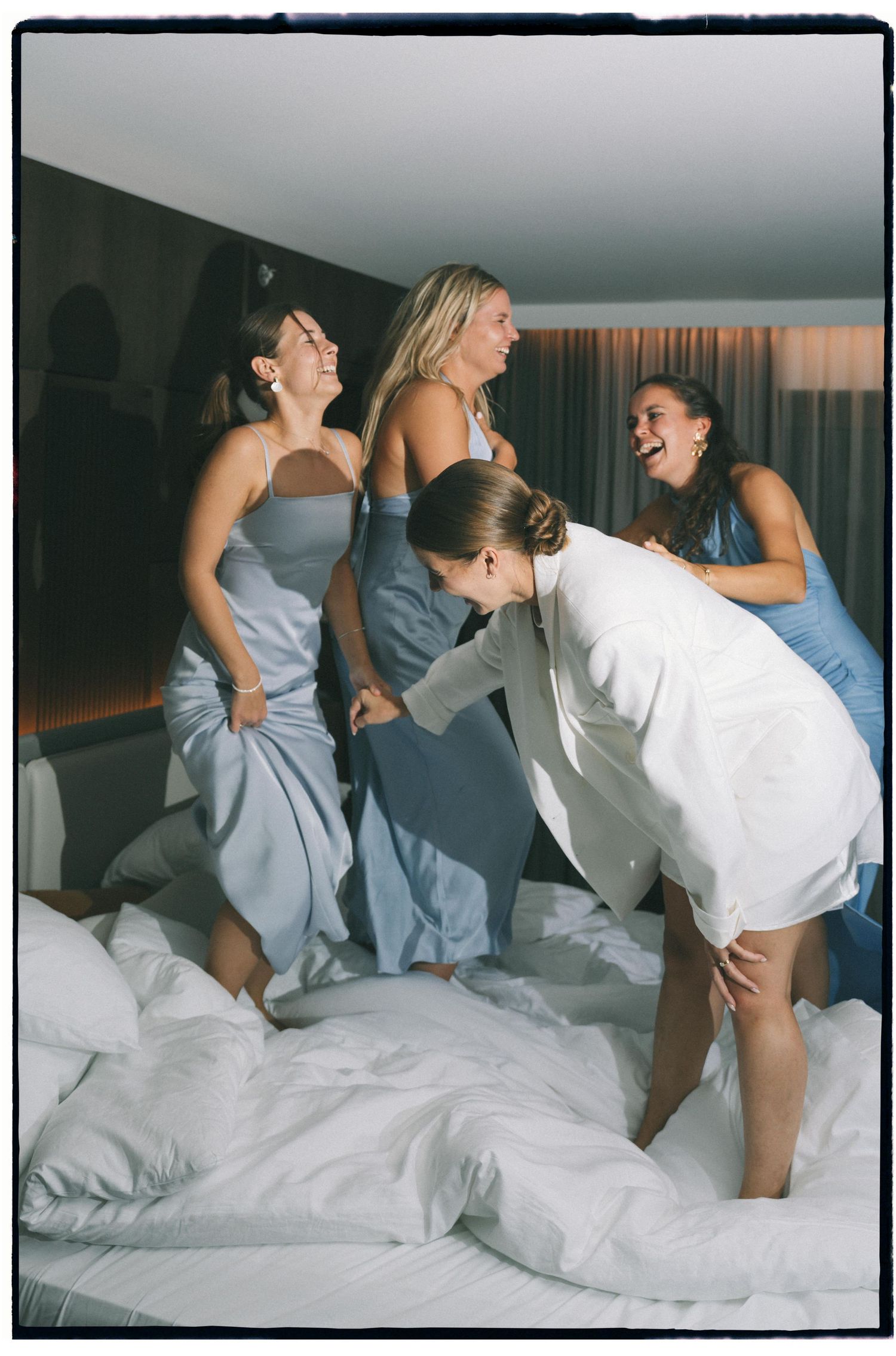 Group in formal attire having fun jumping on a bed together.