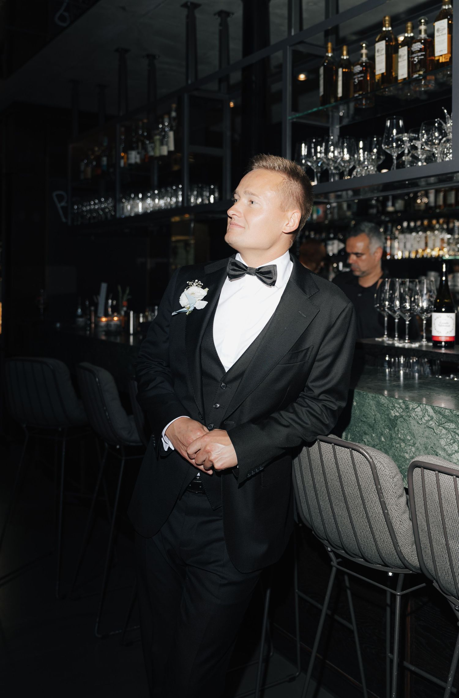 Elegant formal attire at a dimly lit bar with bottles and glassware in background.