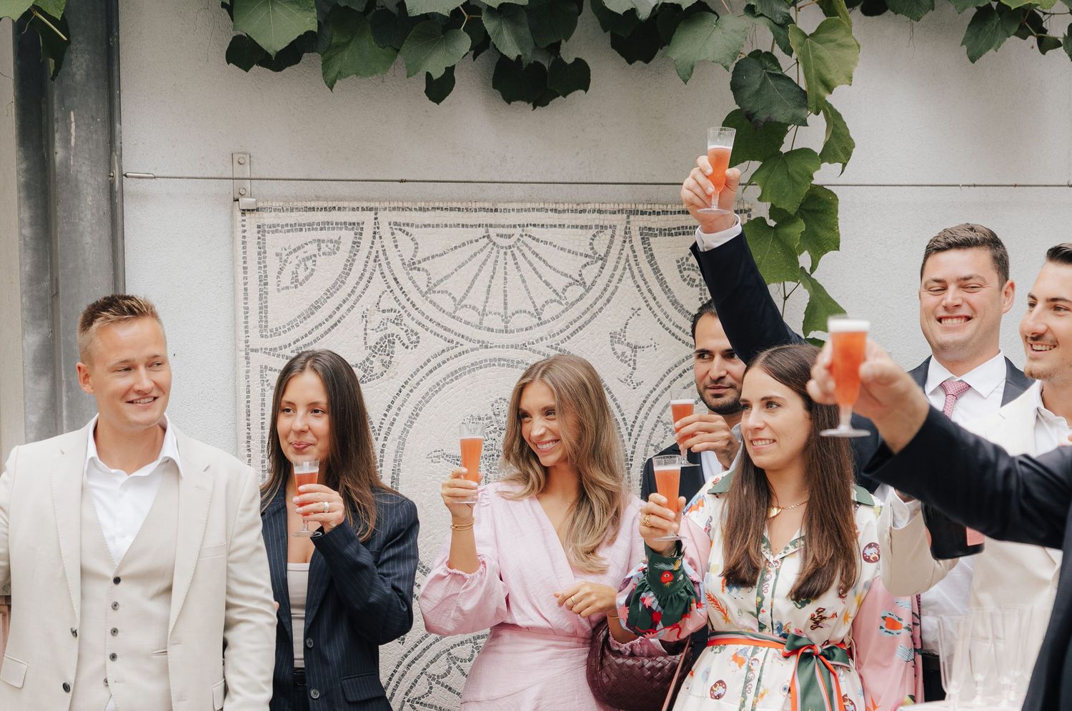 Wedding celebration scene with guests mingling under decorative architectural details and greenery.