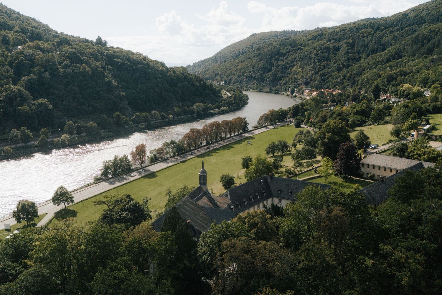 Scenic landscape view of a winding river valley surrounded by forested hills and buildings.