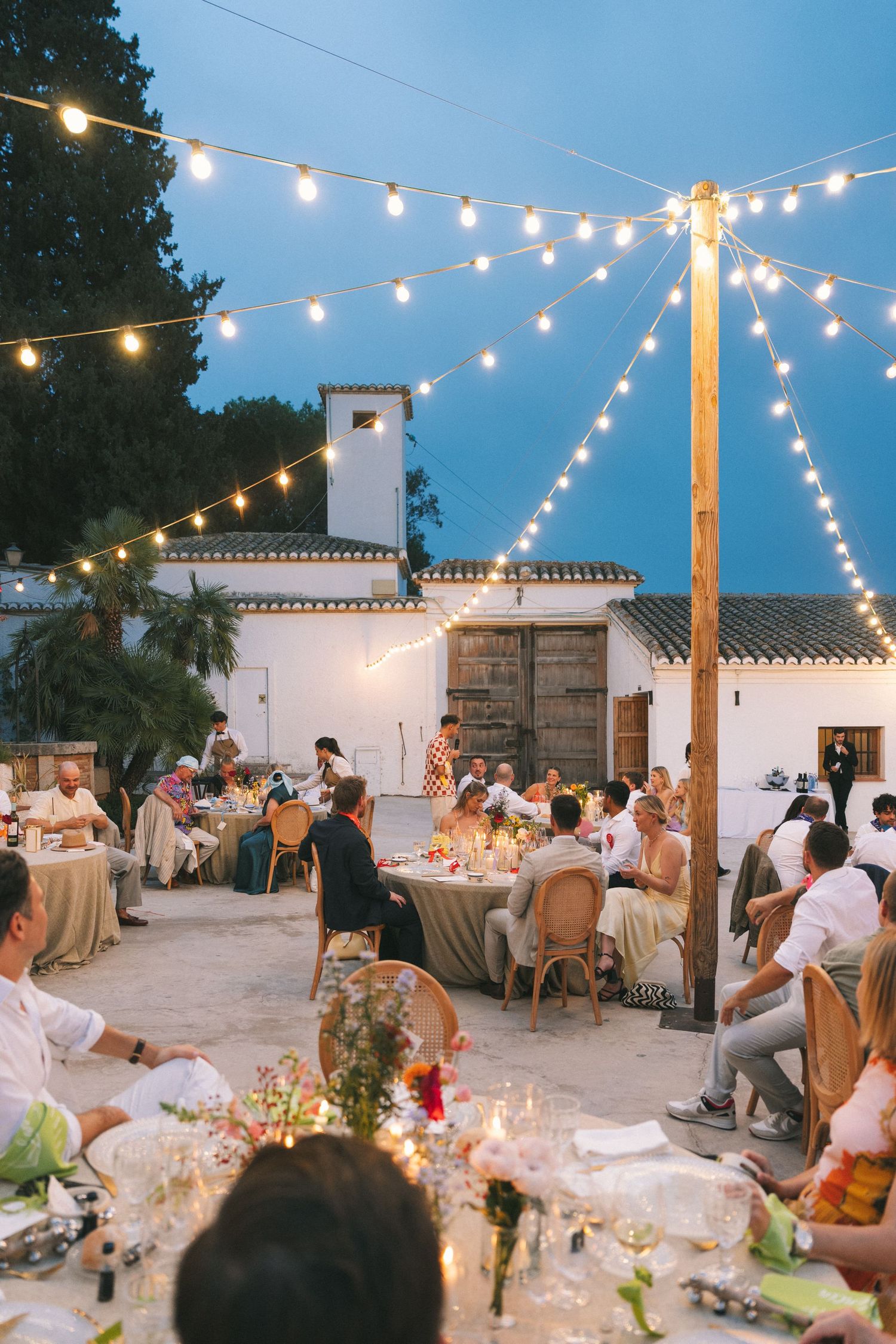 Evening wedding reception with string lights and white buildings creating a romantic atmosphere.