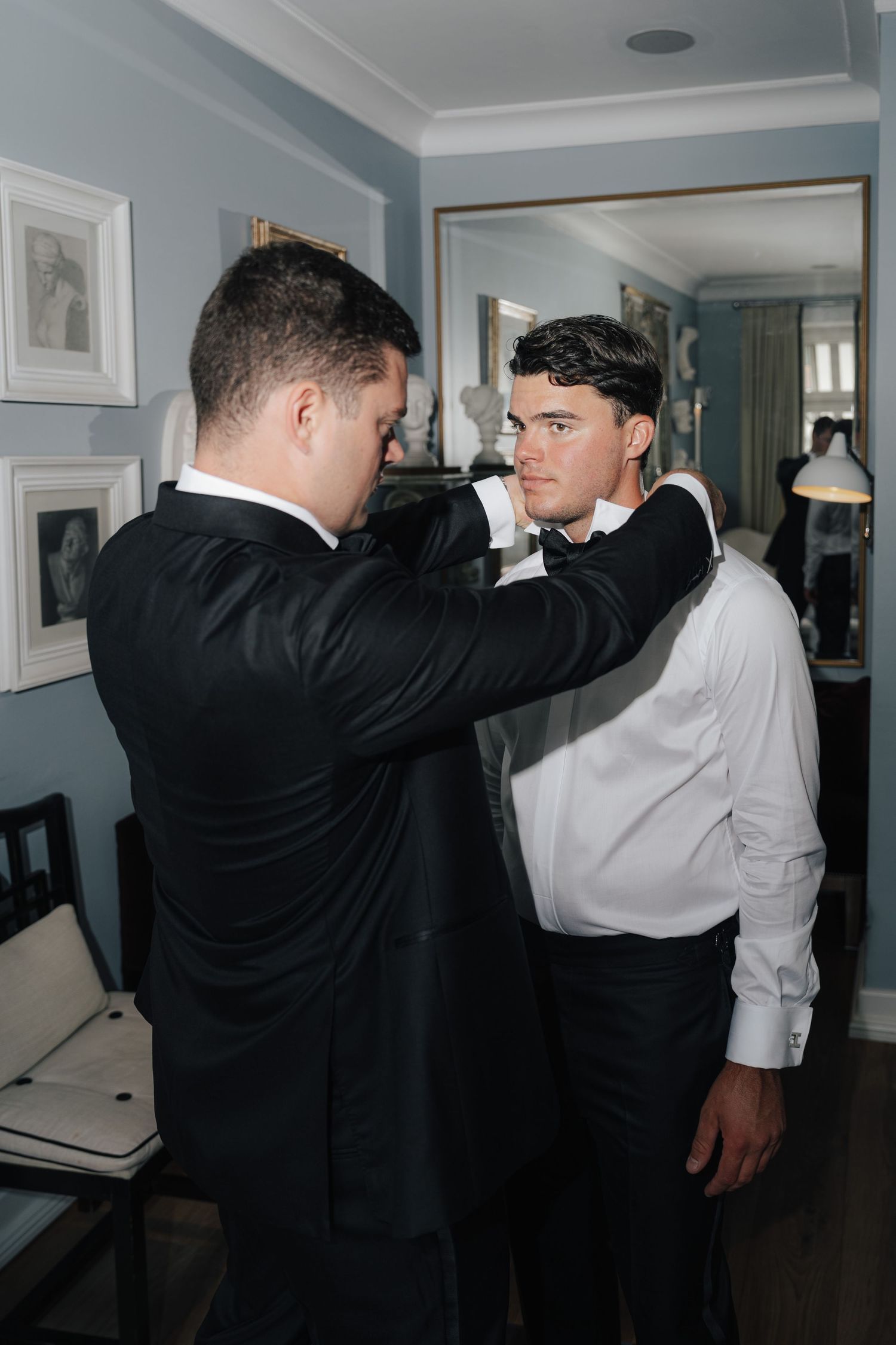 Men in formal attire helping with wedding preparations and adjusting clothing.