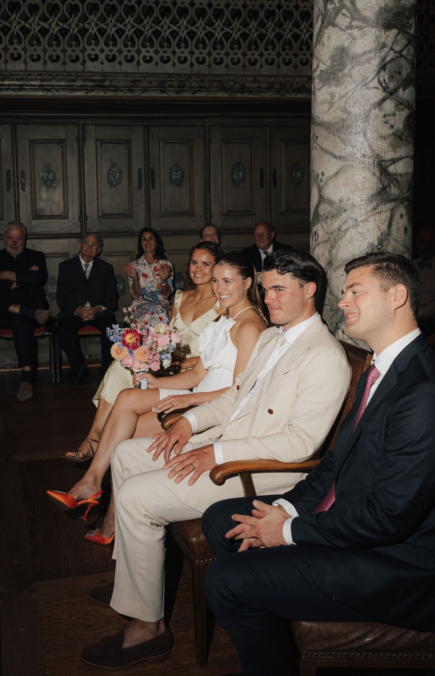 Wedding guests seated in formal attire watching an event in a dimly lit venue.