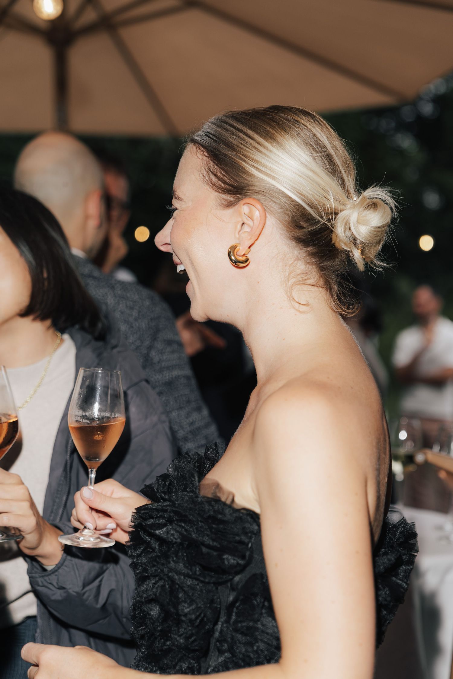 Wedding reception guests laughing and socializing under an outdoor tent with ambient lighting.