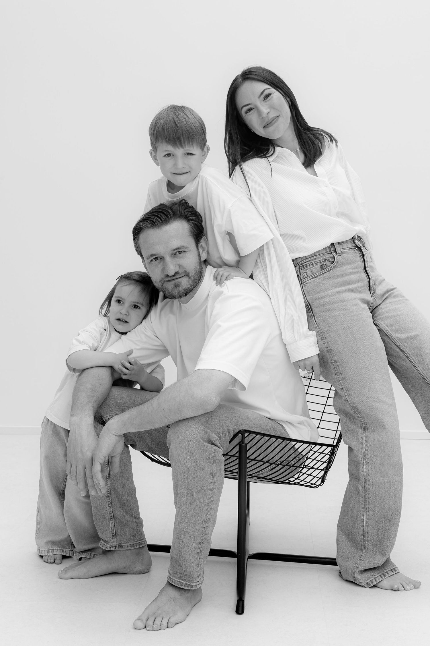 Black and white family portrait of parents and two children posing together on a chair in a studio.
