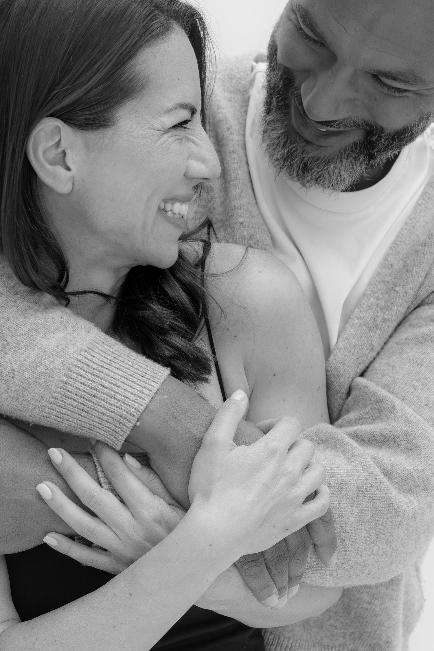 Black and white photo of a laughing couple embracing warmly, the man wrapping his arms around the smiling woman.