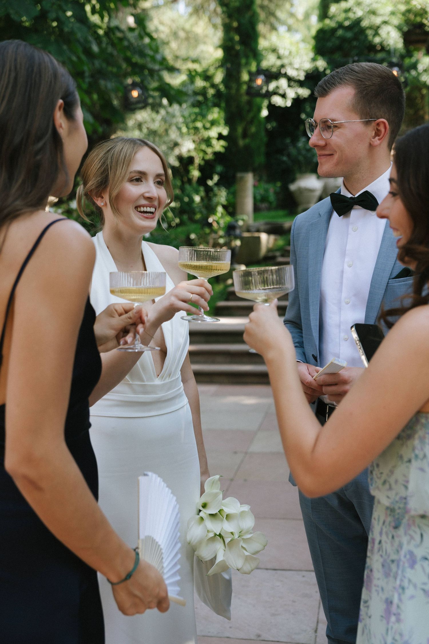 Bride and groom toasting champagne with guests outdoors at elegant garden wedding reception.