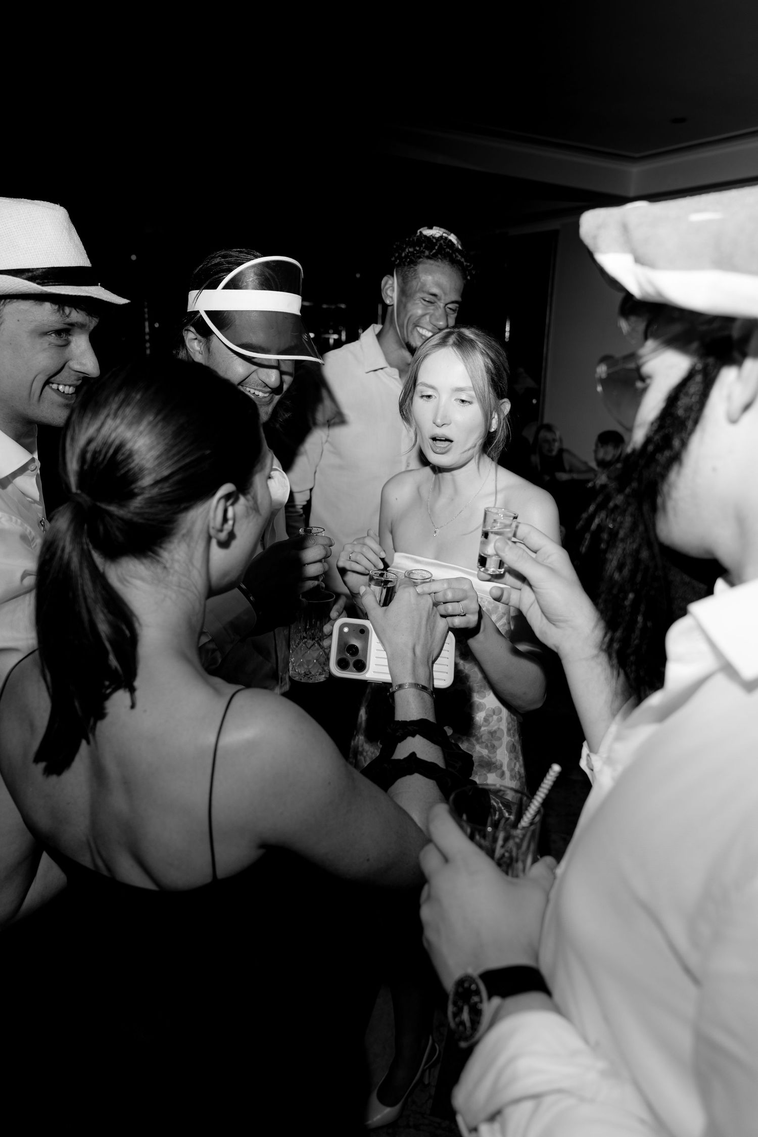Black and white photo of a group of people socializing at a party, wearing hats and holding drinks.