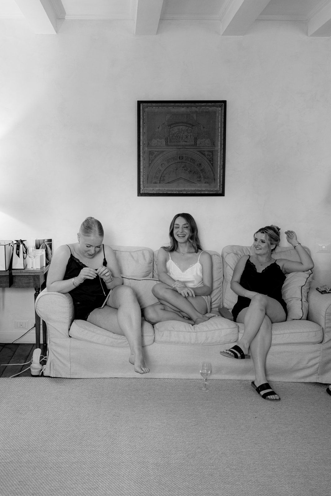 Three women relaxing on a white sofa in black and white photo, one knitting, one smiling, one posing.