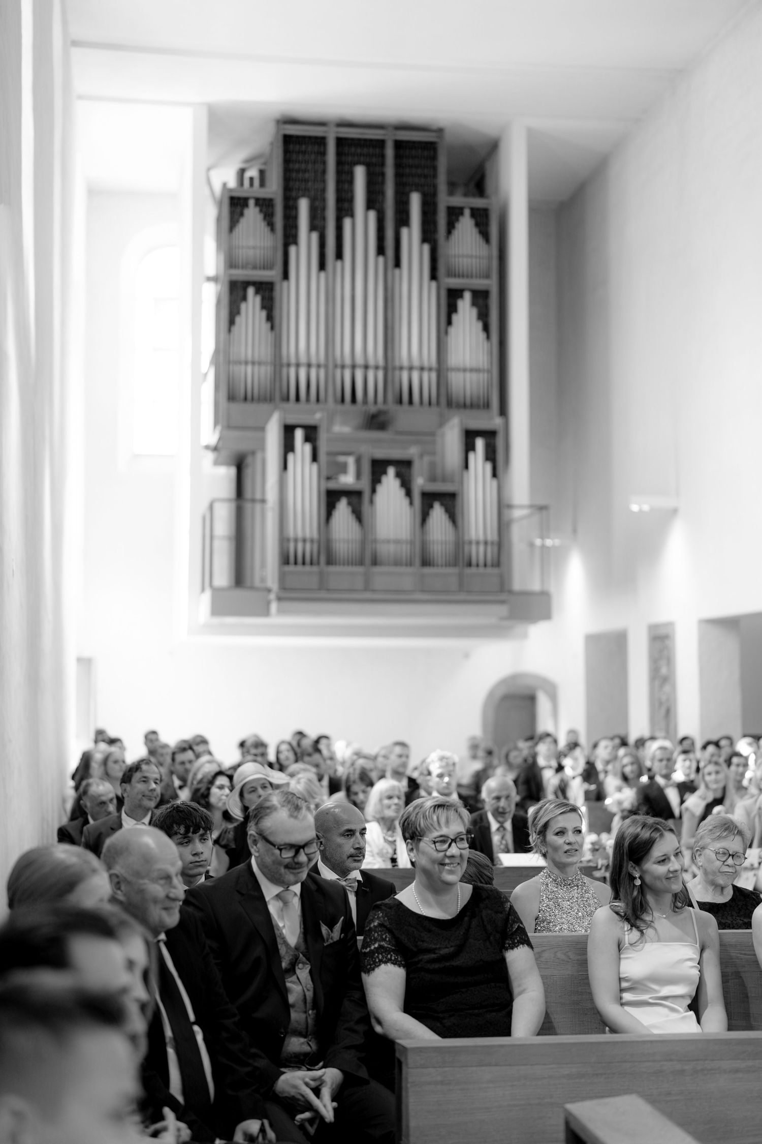 Church interior filled with wedding guests and featuring a prominent pipe organ on the wall.