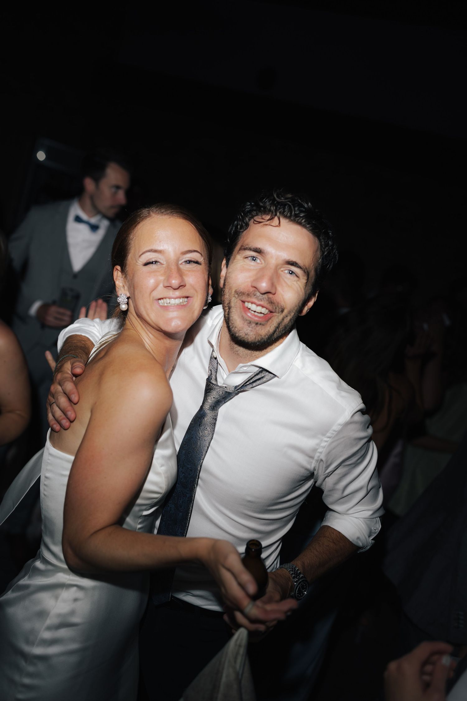 Party guests dancing and embracing on a dark dance floor.