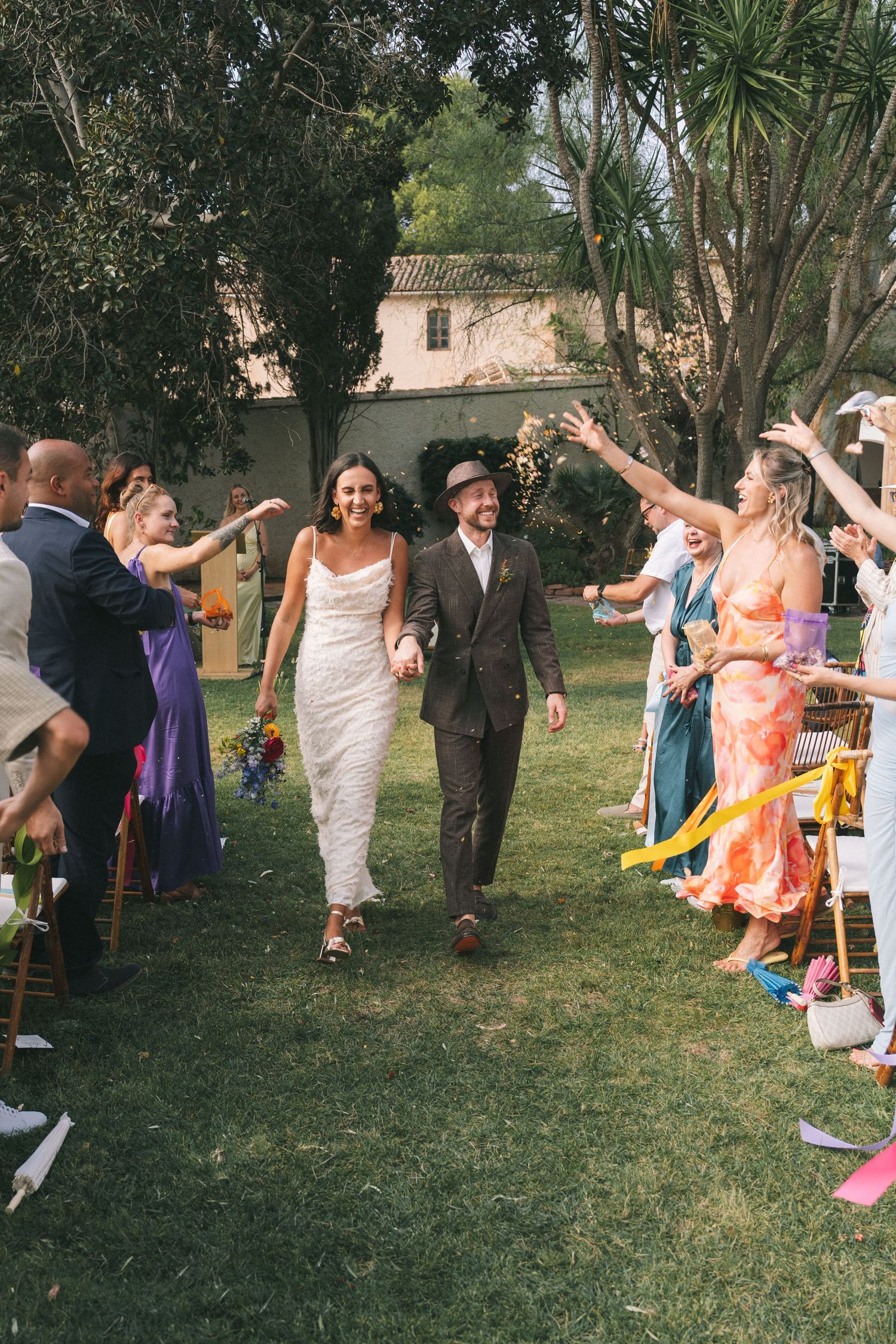Wedding party celebrates with dancing and laughter in a garden setting.
