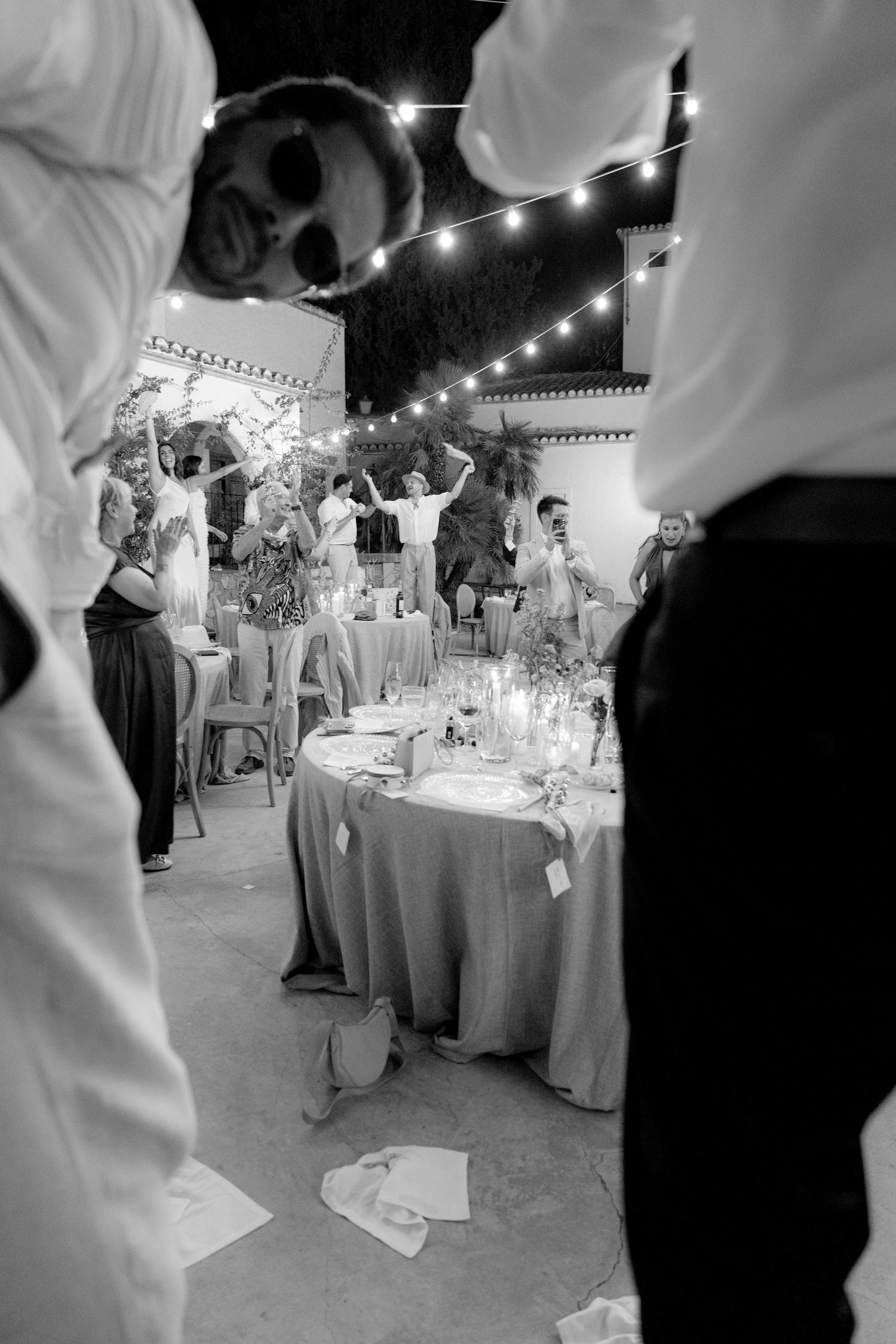 Wedding reception tables decorated with string lights and white linens create an elegant evening atmosphere.