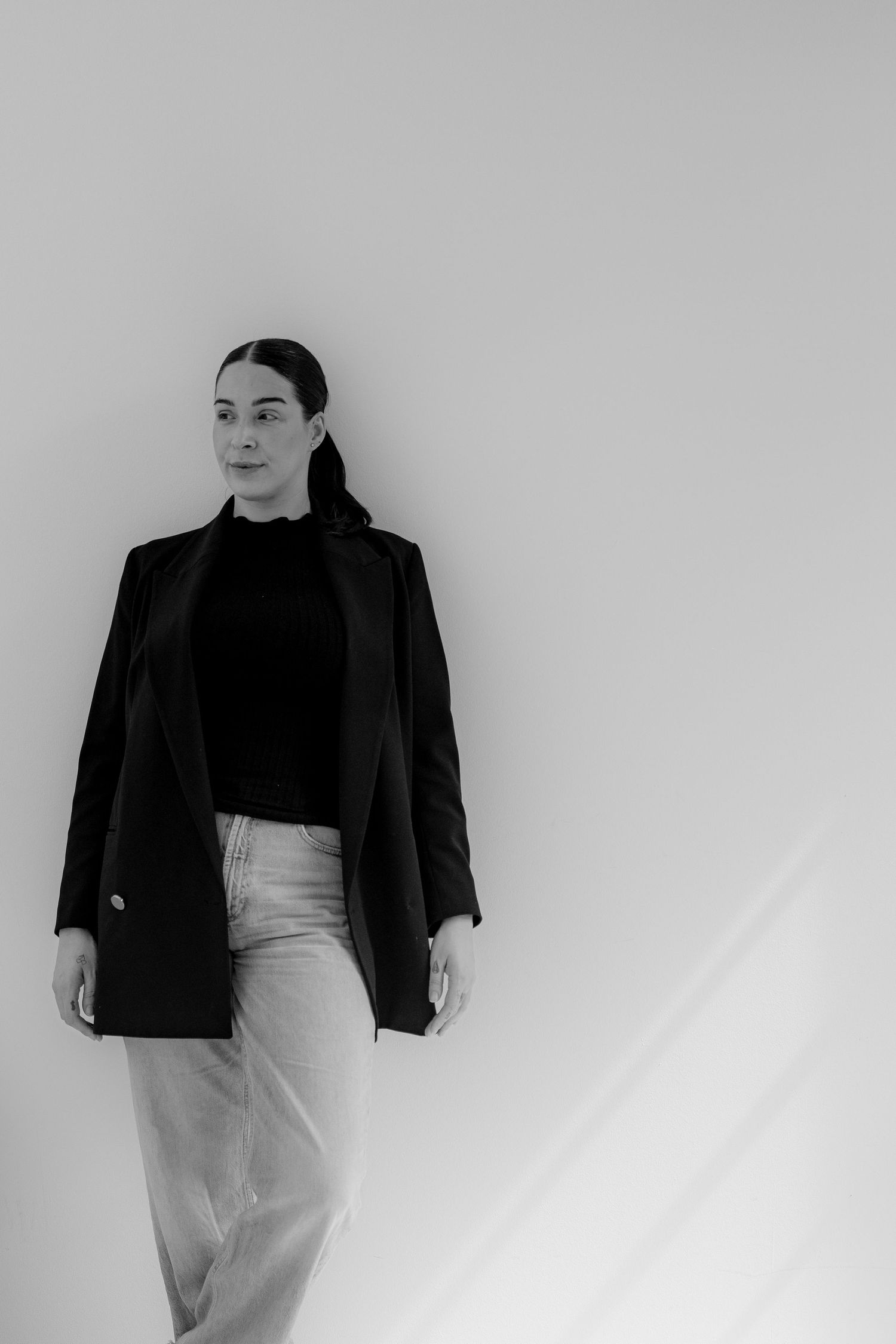 Black and white portrait of a woman in a black blazer and turtleneck, standing against a light background.
