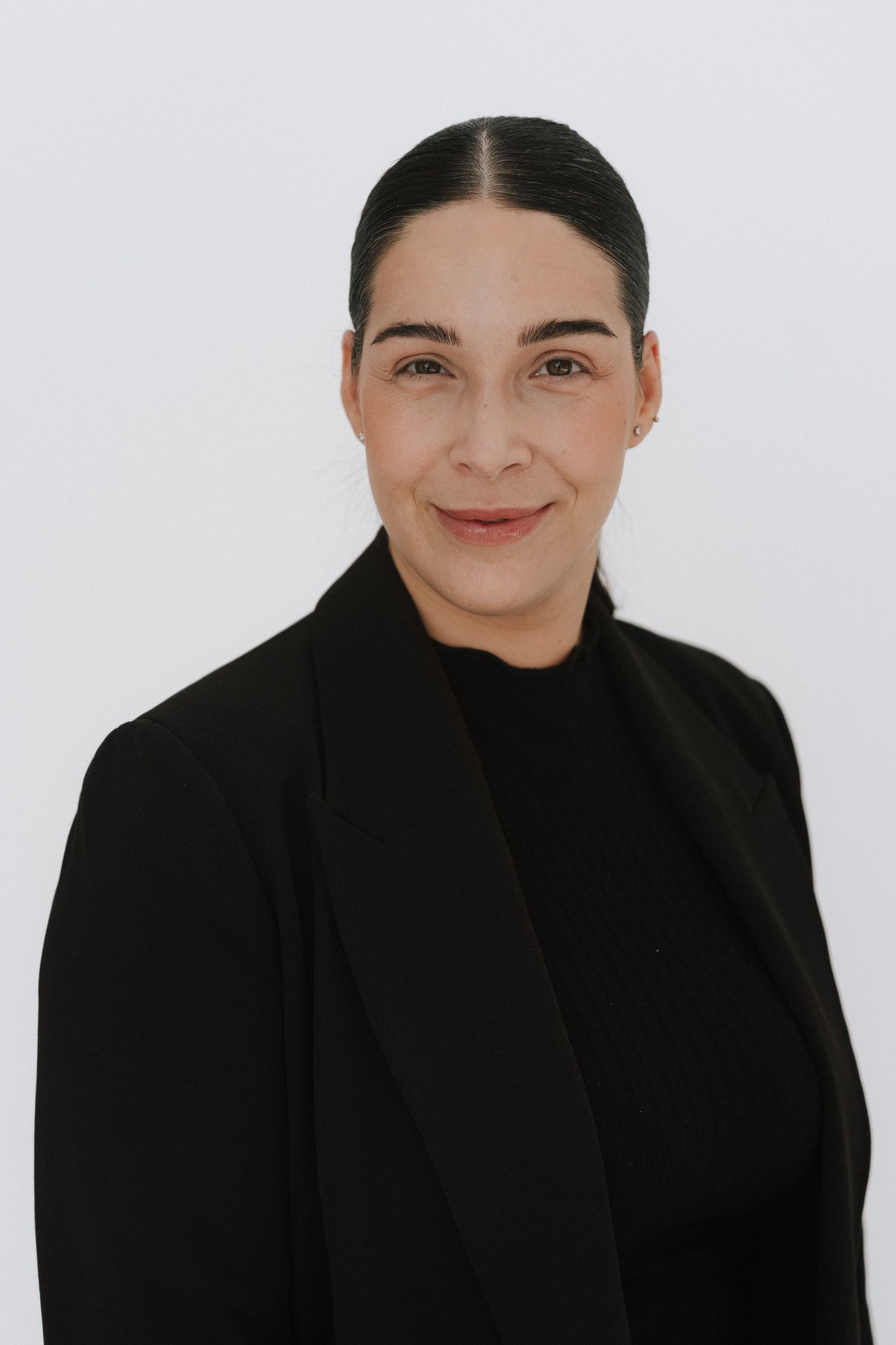 Professional woman in black blazer and turtleneck smiling confidently against white background.