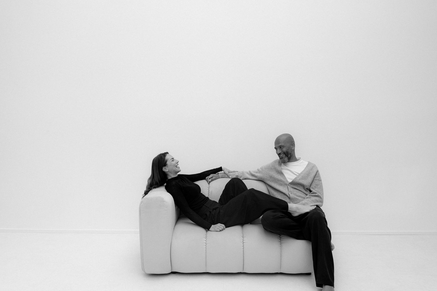 Black and white photo of a couple relaxing on a white sofa, woman lying down while man sits smiling at her.