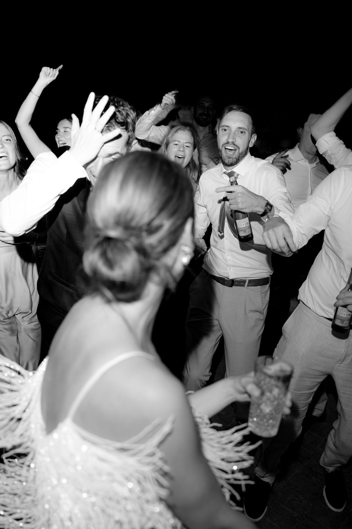 Black and white photo of wedding guests dancing with raised hands at a reception.
