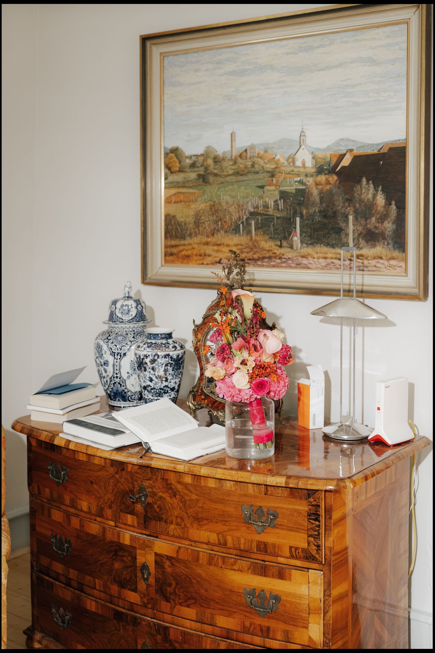 Vintage wooden dresser decorated with flowers, blue and white porcelain, and landscape painting above.