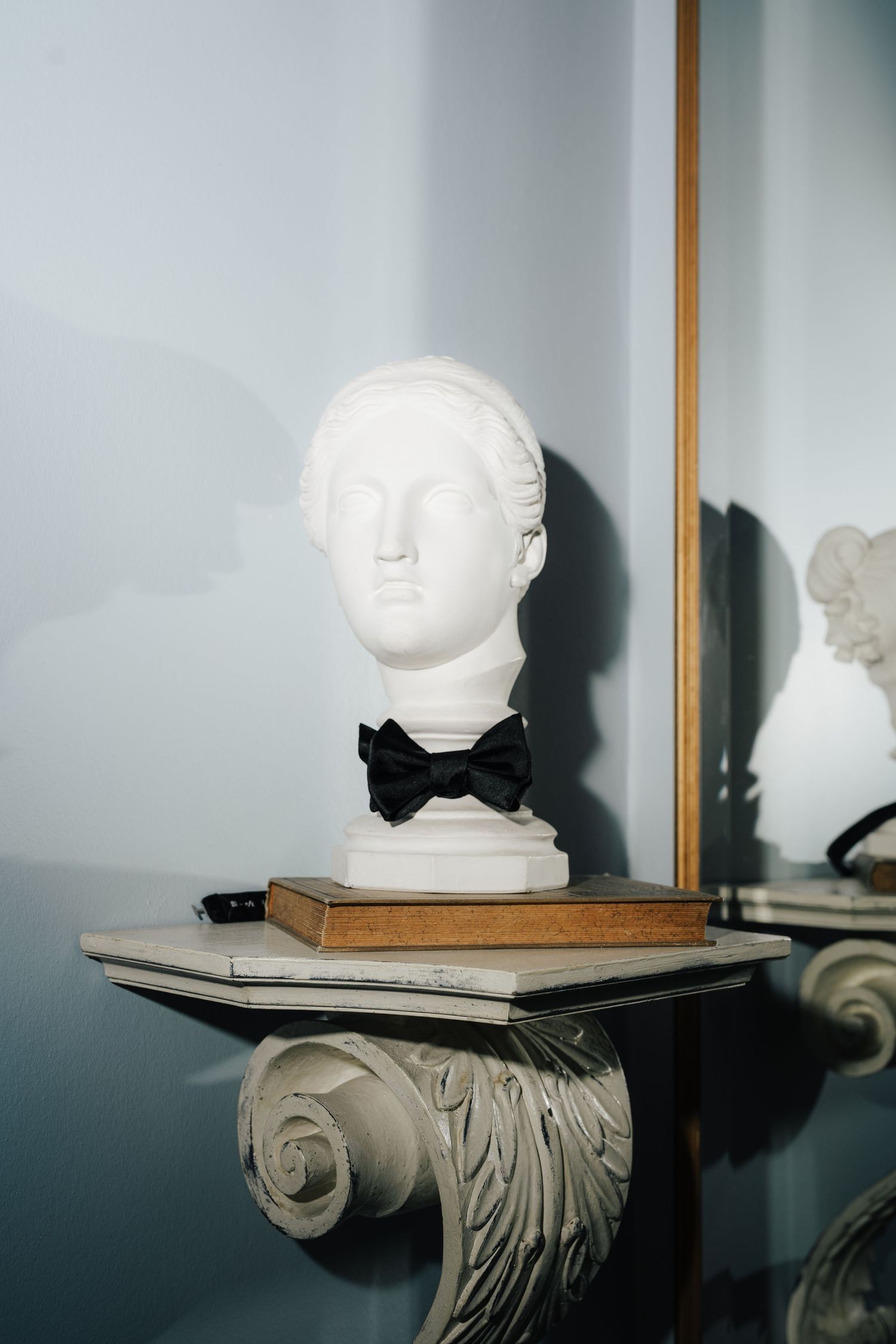 White sculptural bust displayed on an ornate wall-mounted shelf against a light colored wall.
