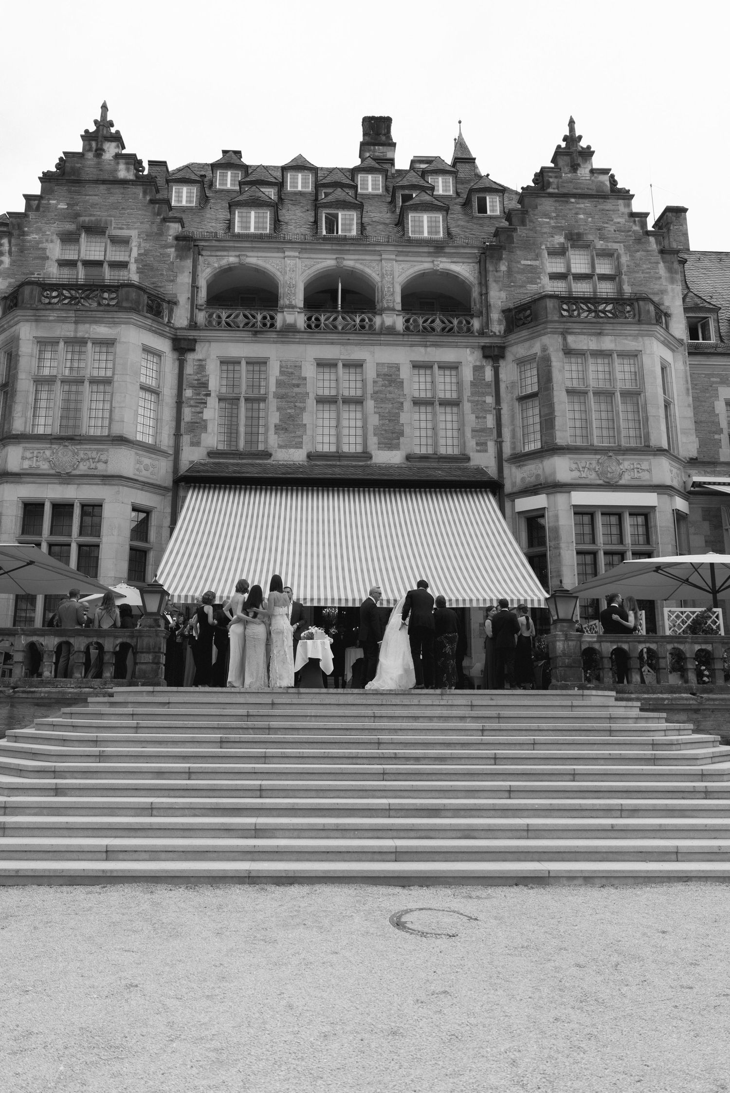 Black and white photo of a wedding ceremony on grand stone steps of a historic European mansion.