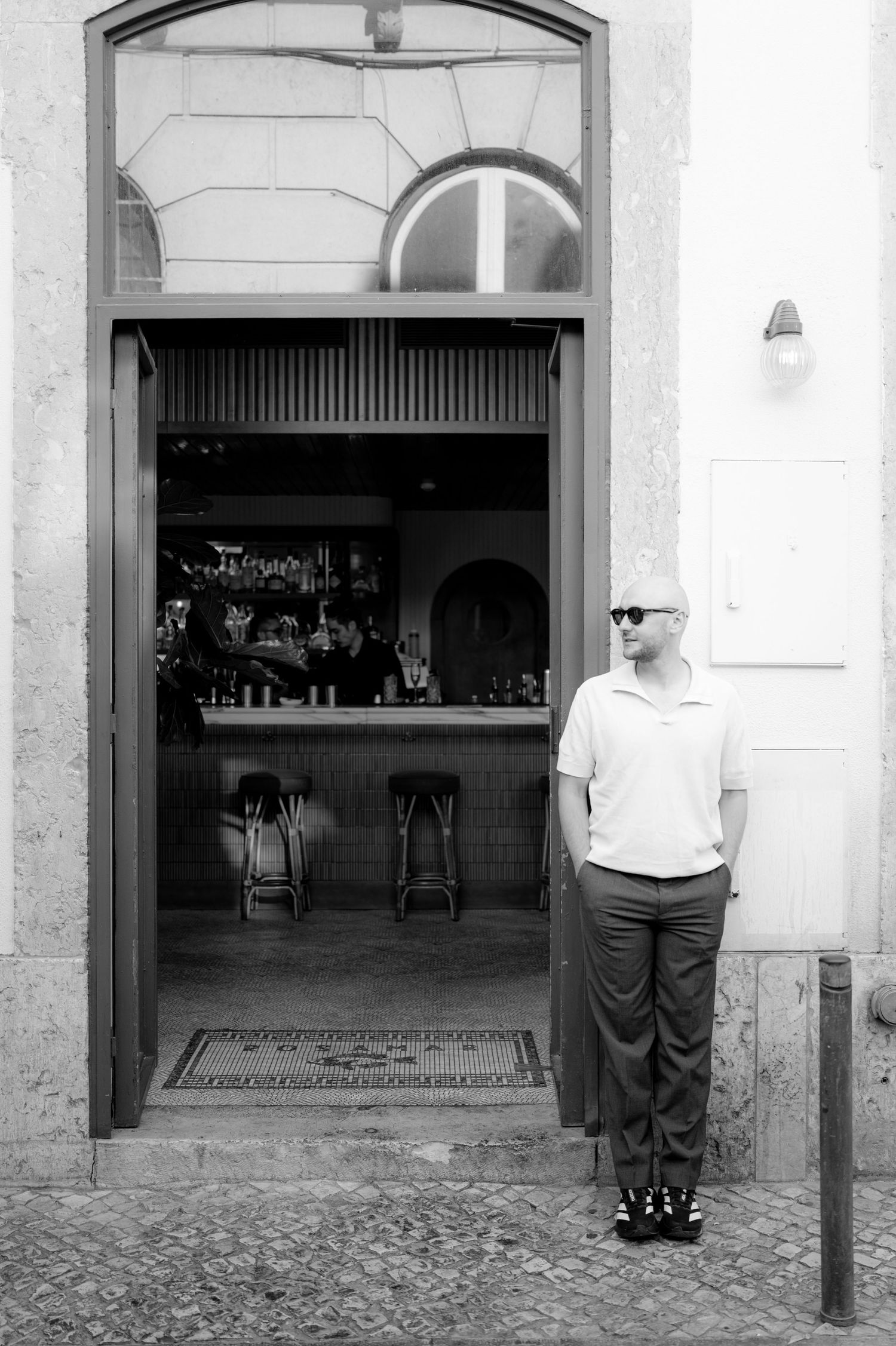 Black and white photograph of storefront entrance with bar visible inside.