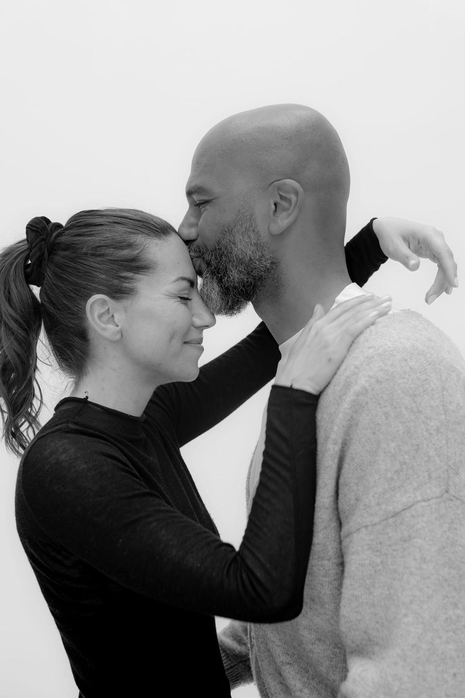 Black and white photo of a couple sharing a tender moment, woman smiling as man leans in to kiss her.