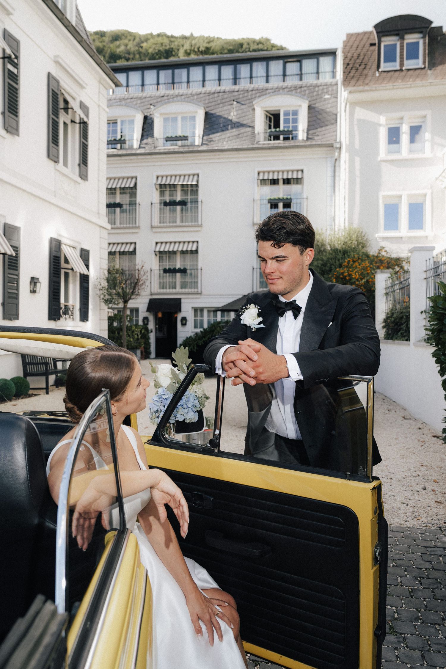 A couple poses with a vintage yellow car during their wedding photoshoot.