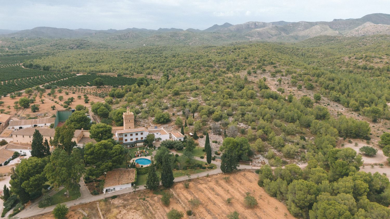 Aerial view of Mediterranean village nestled in rolling hills with swimming pool visible.