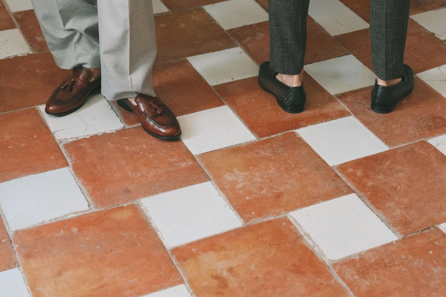 Various dress shoes and formal footwear on a terracotta and white checkered floor.