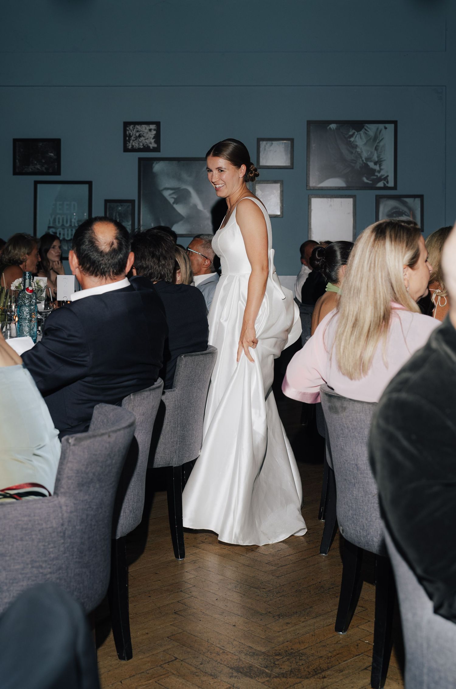 Elegant wedding reception scene with guests seated at tables and artwork on blue walls.