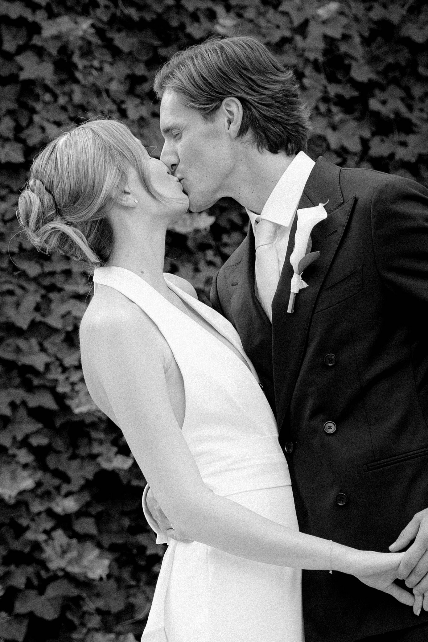 Black and white photo of a bride and groom sharing a romantic kiss on their wedding day outdoors.