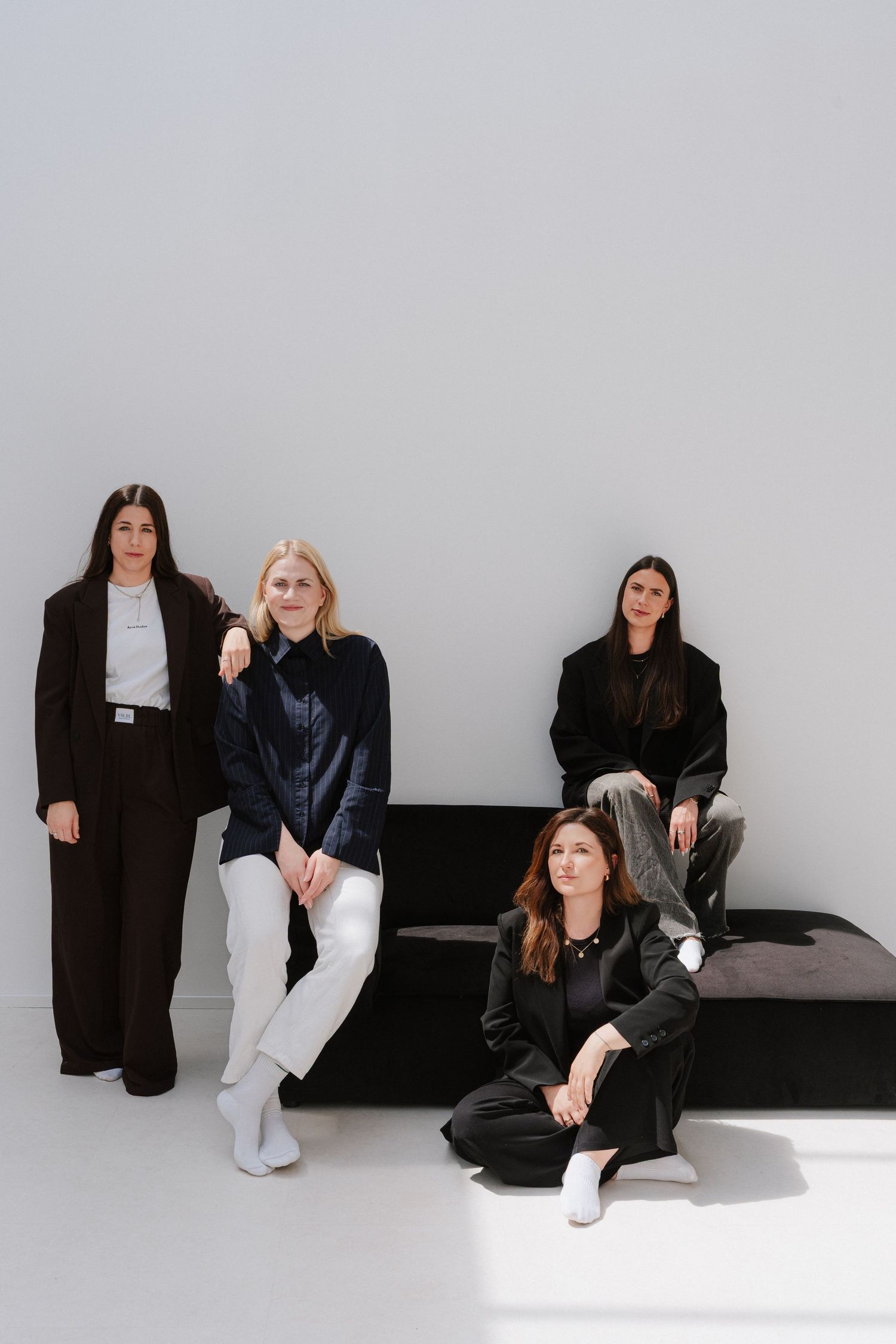Four stylish women in black and white outfits posing together in a minimalist white studio setting.