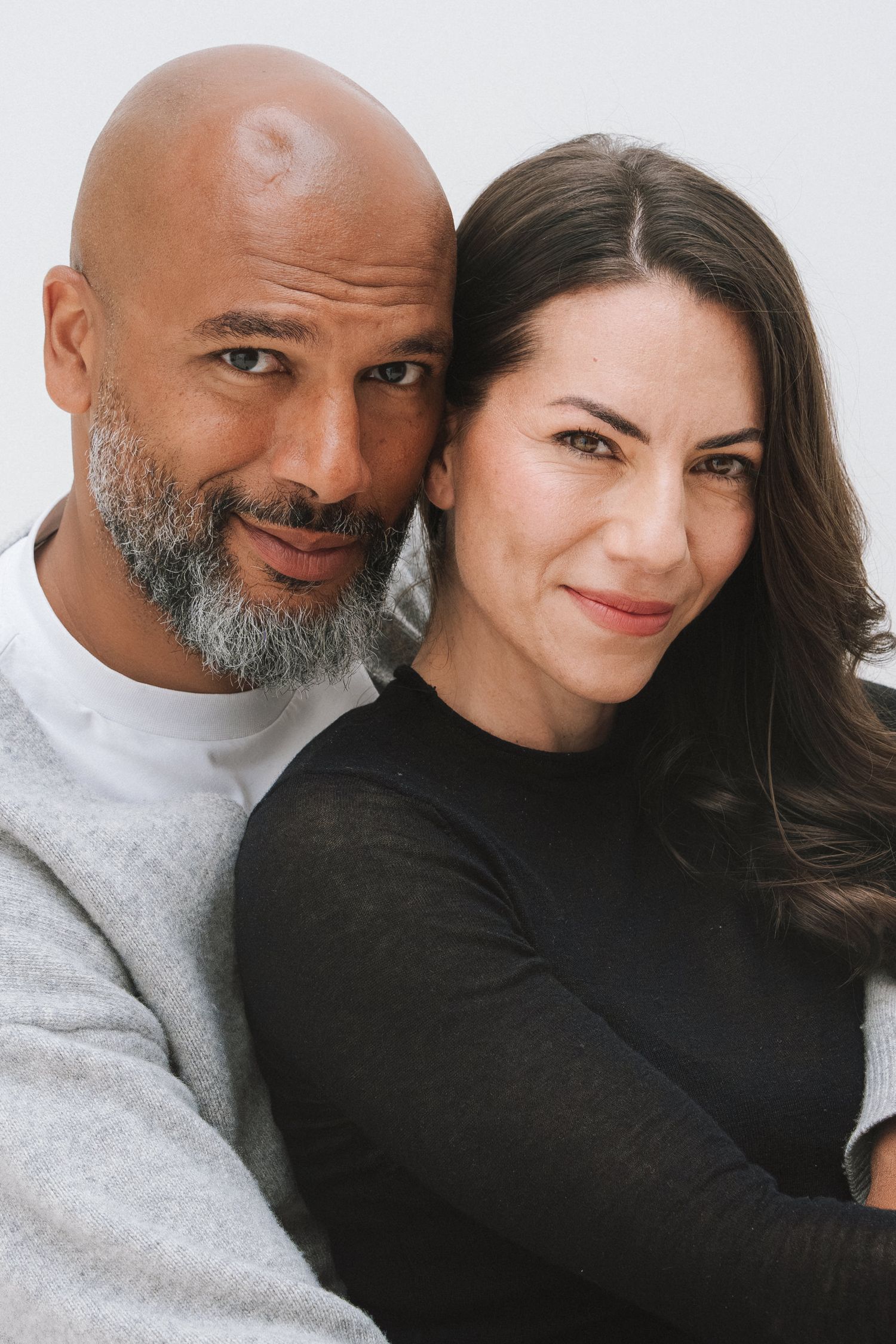 A bald man with a gray beard and a brunette woman smile warmly together in a close portrait photo.