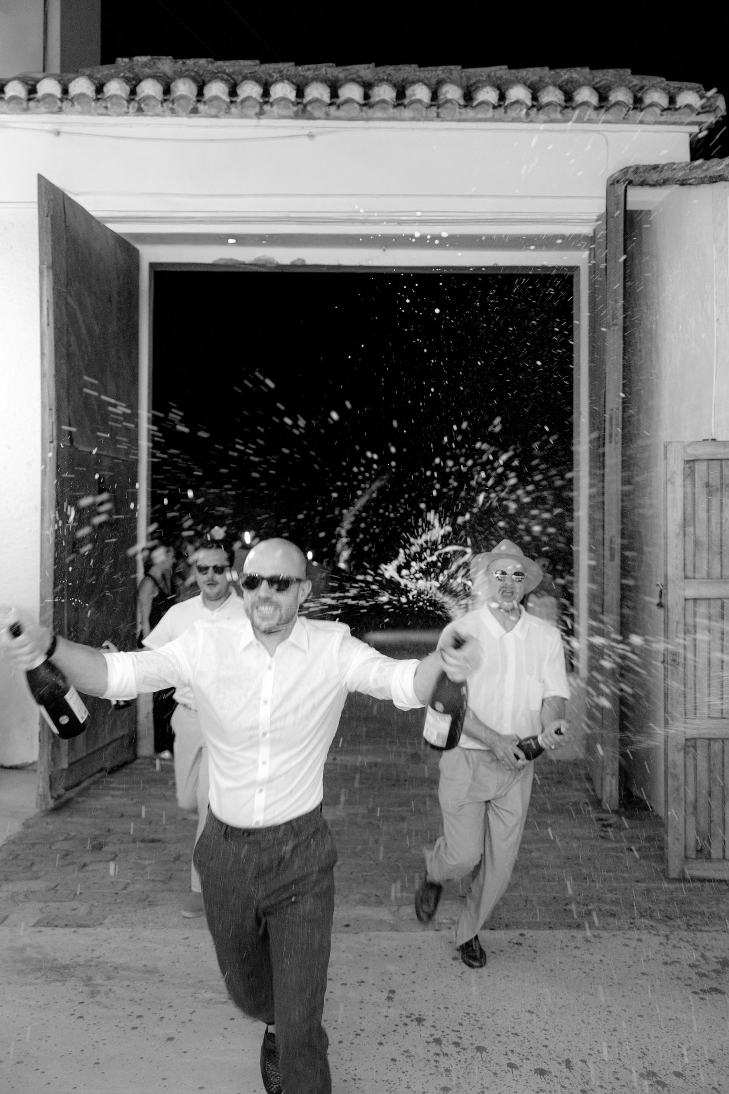 People jumping and celebrating in front of a white Spanish-style building entrance.