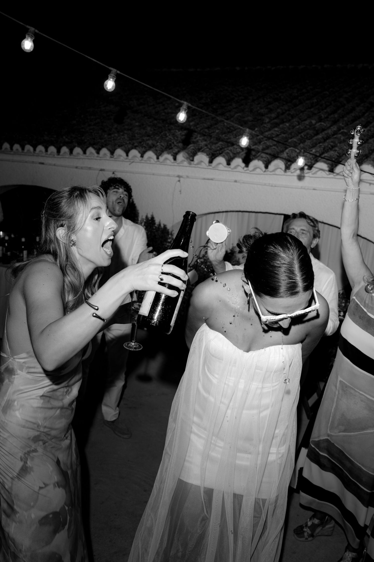 Wedding guests taking shots of alcohol at an outdoor reception under string lights.