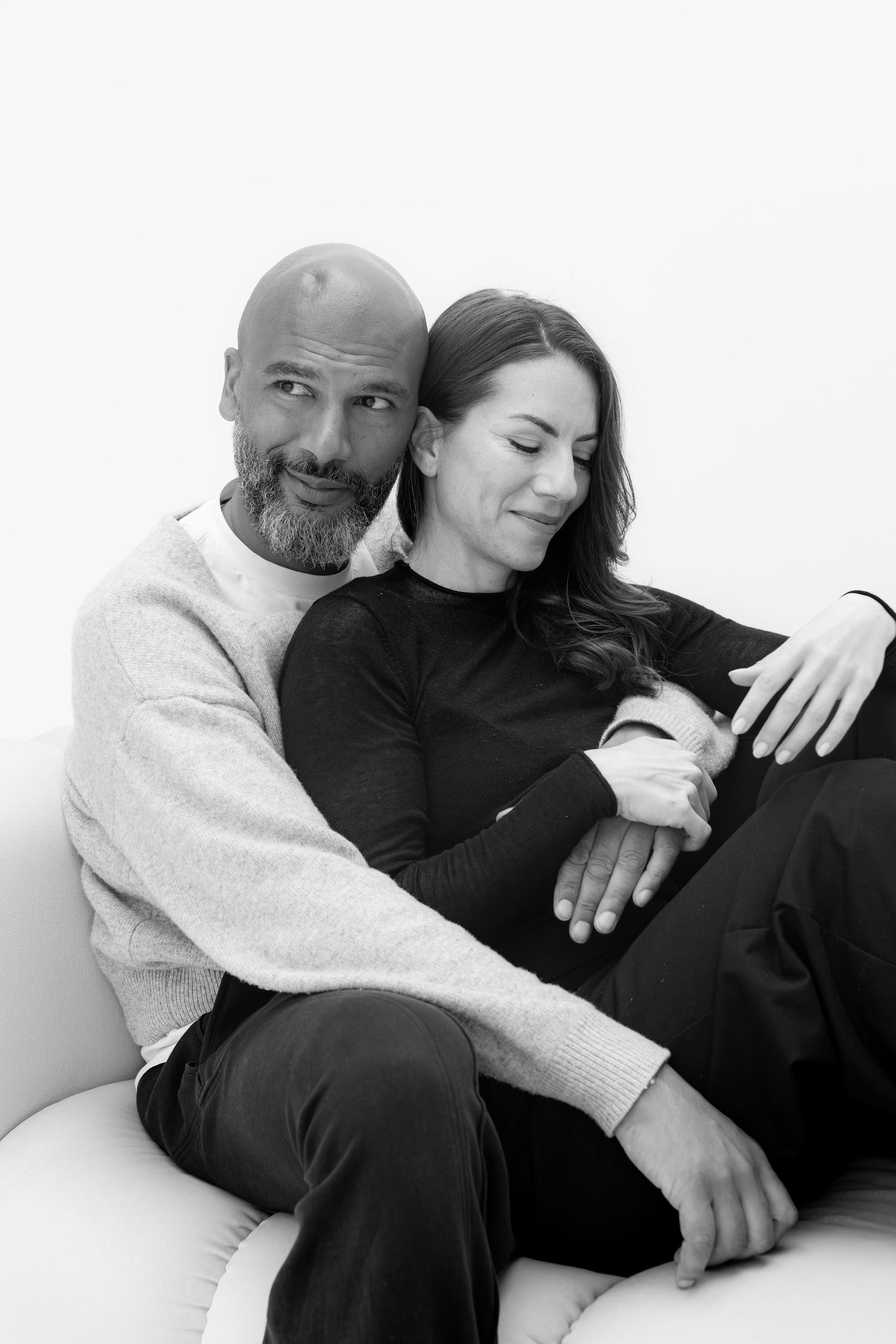Black and white portrait of a couple sitting together on a sofa, smiling and embracing warmly.
