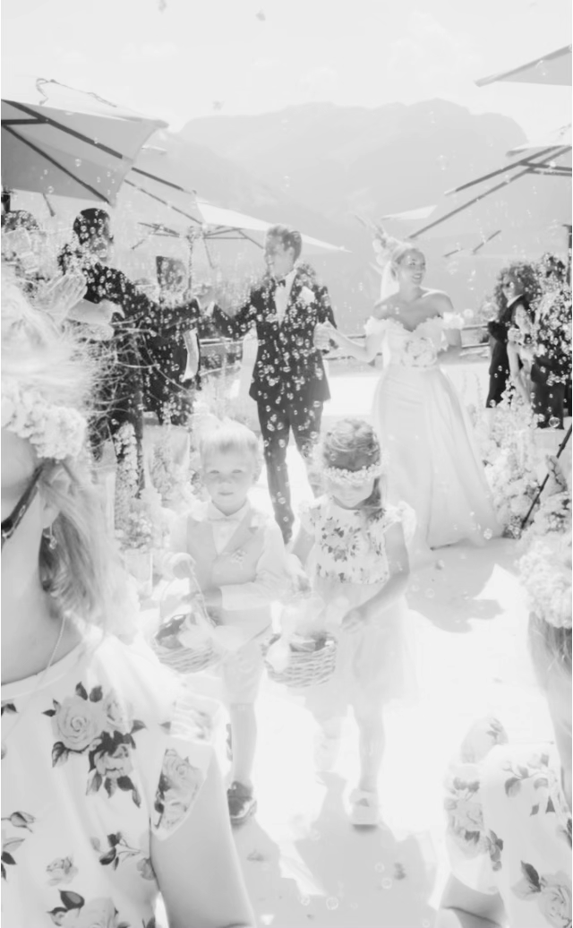 Bridesmaids in white dresses pose playfully in a garden setting with bright sunlight.