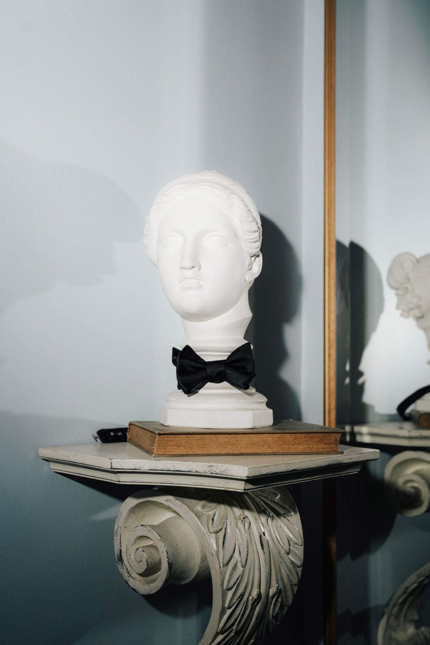 White sculptural bust on ornate wall mounted shelf against blue wall.