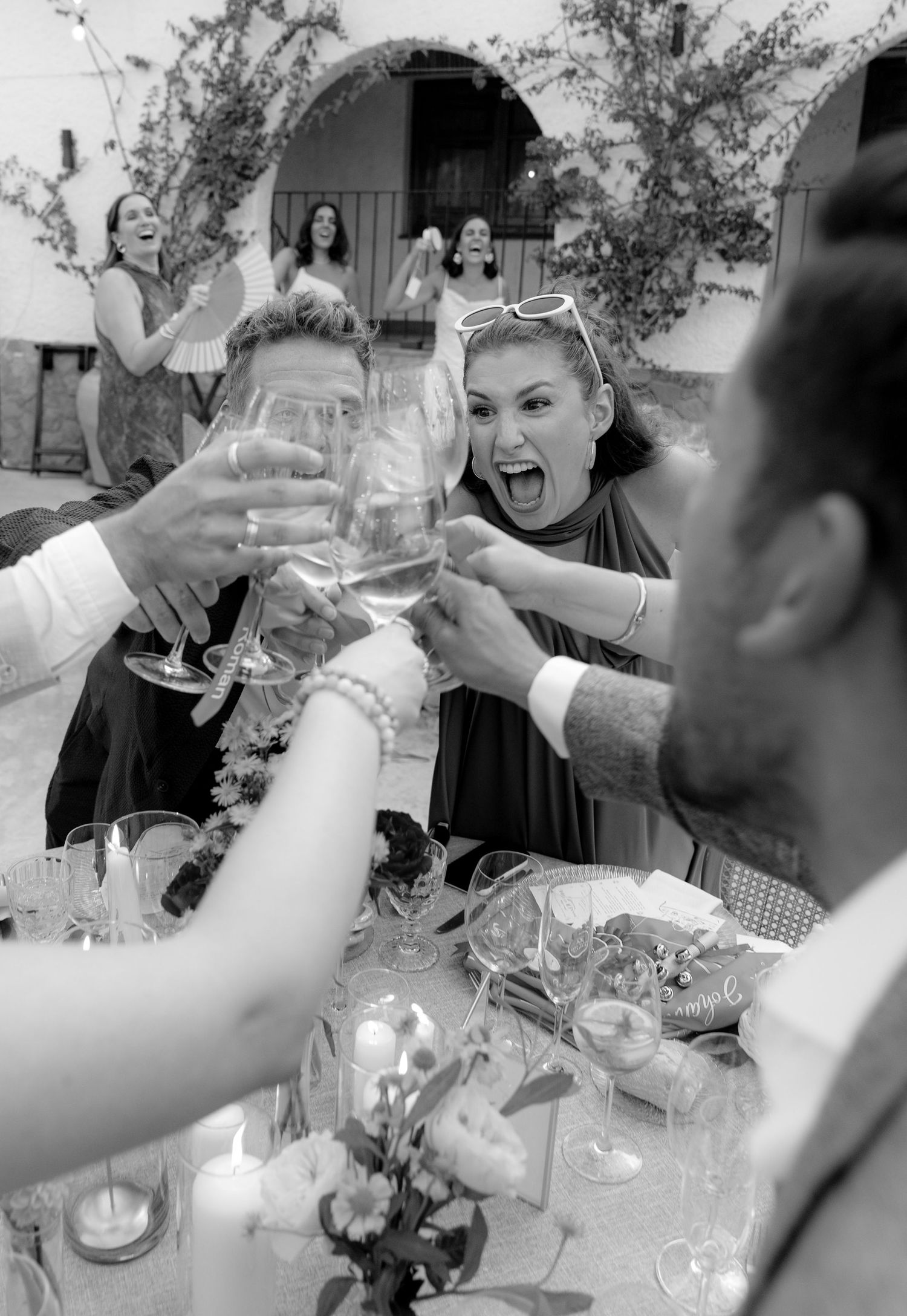 Black and white photo of guests toasting with wine glasses at an outdoor reception.
