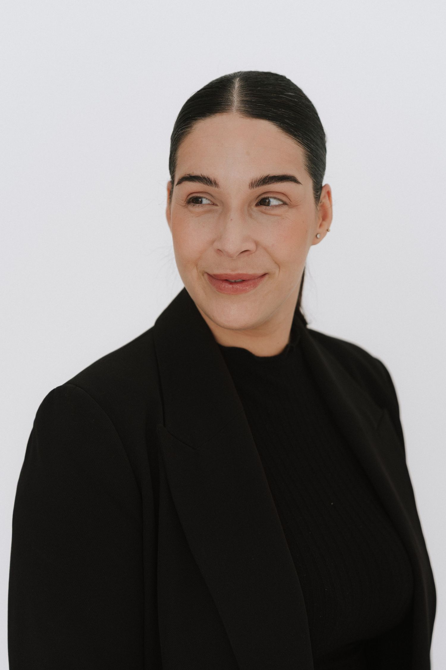 Professional woman in black blazer and turtleneck with sleek hair, posing against white background.