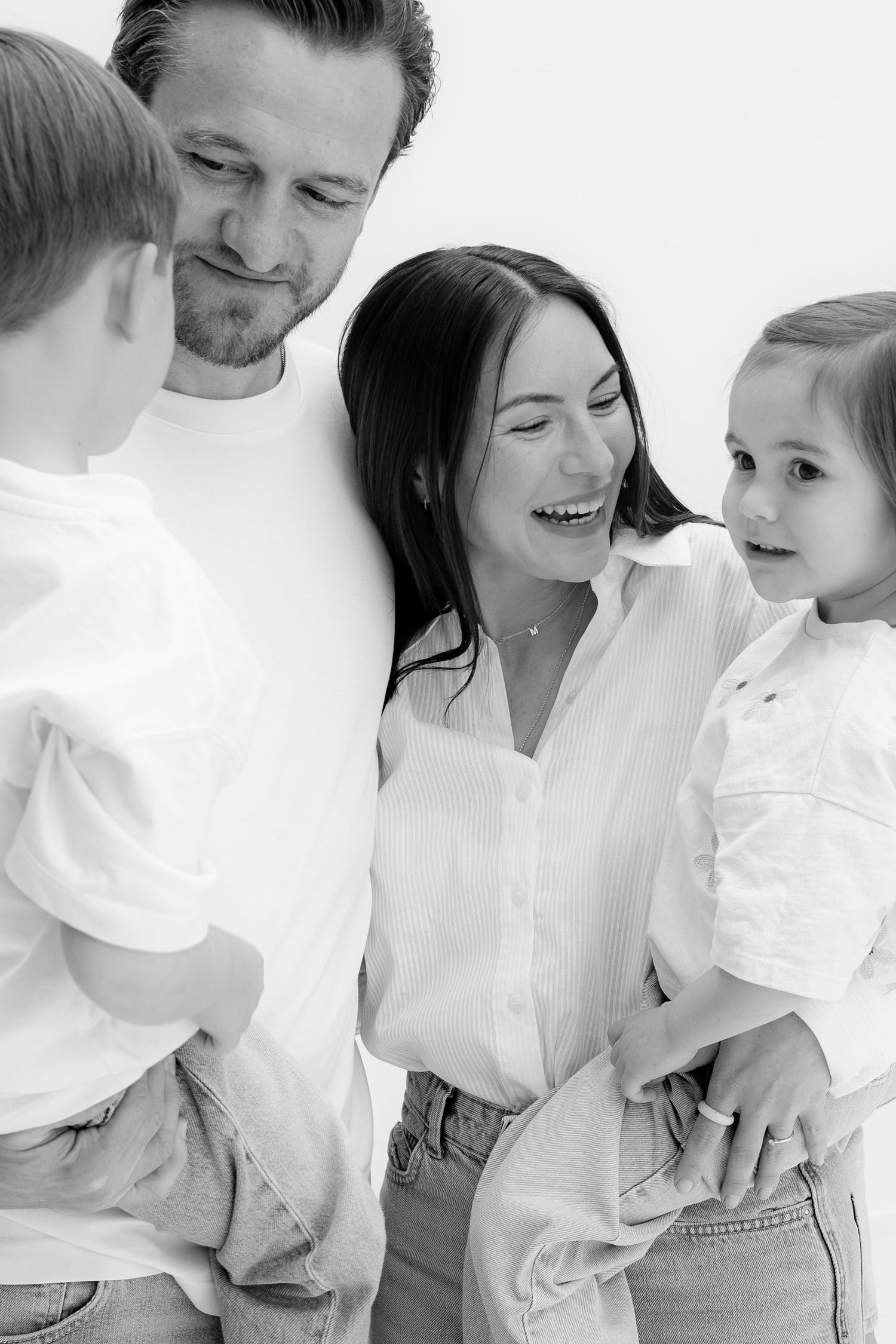 Black and white family portrait of parents smiling with two young children in white shirts and jeans.