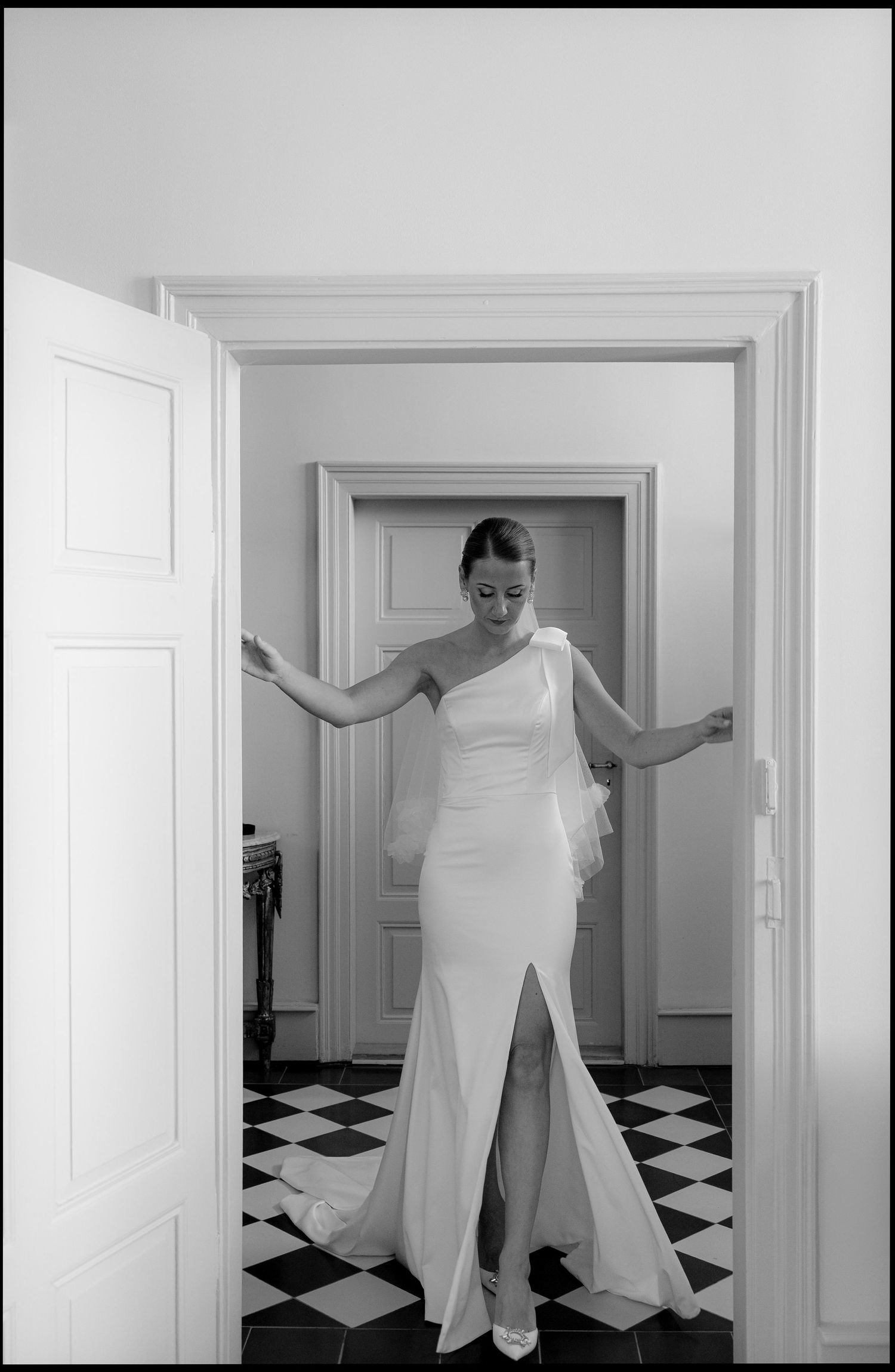 Black and white sequence showing someone in a white dress moving through a checkered floor hallway.