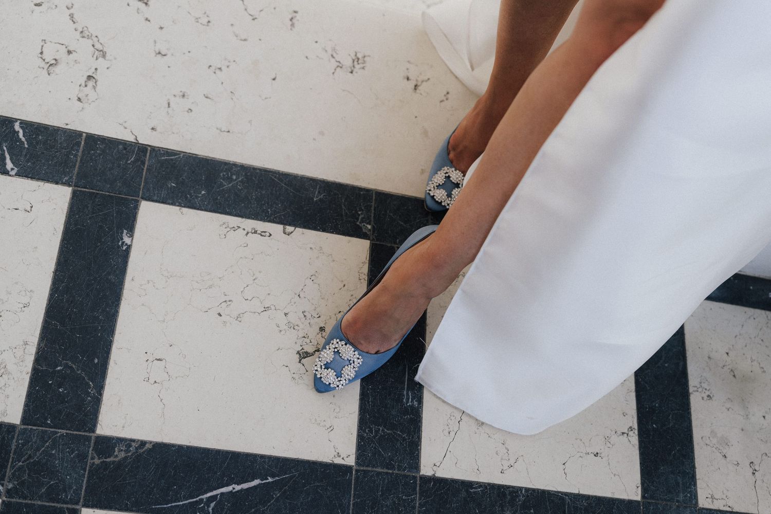 Close-up shot of sparkly blue wedding shoes on a black and white checkered floor.