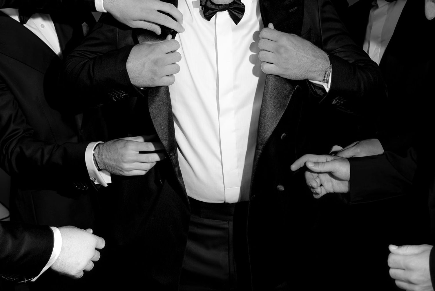 Black and white photo of formal event preparations with people adjusting bowties.