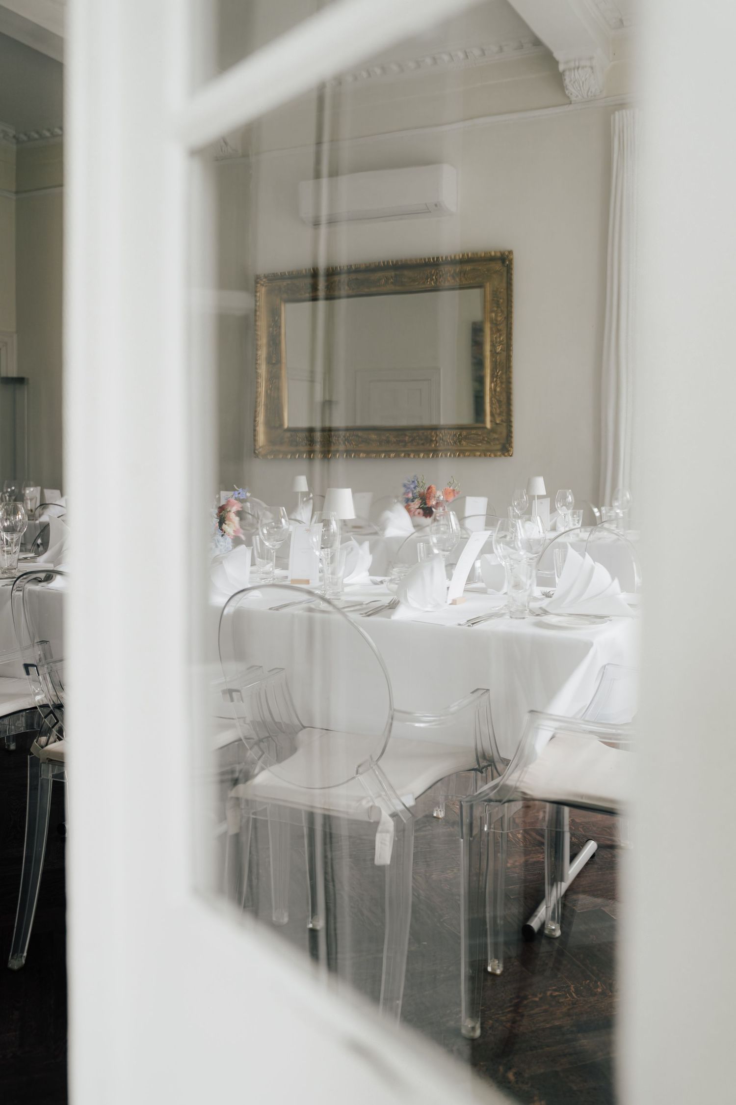 Elegant white dining tables set with glassware and place settings in a bright room with natural light.