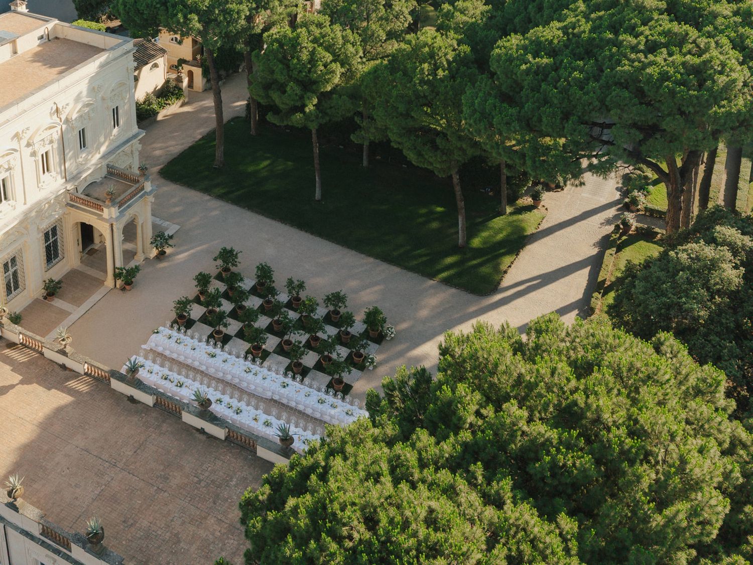 Aerial view of an elegant villa courtyard with white chairs arranged for an outdoor ceremony surrounded by lush green trees.