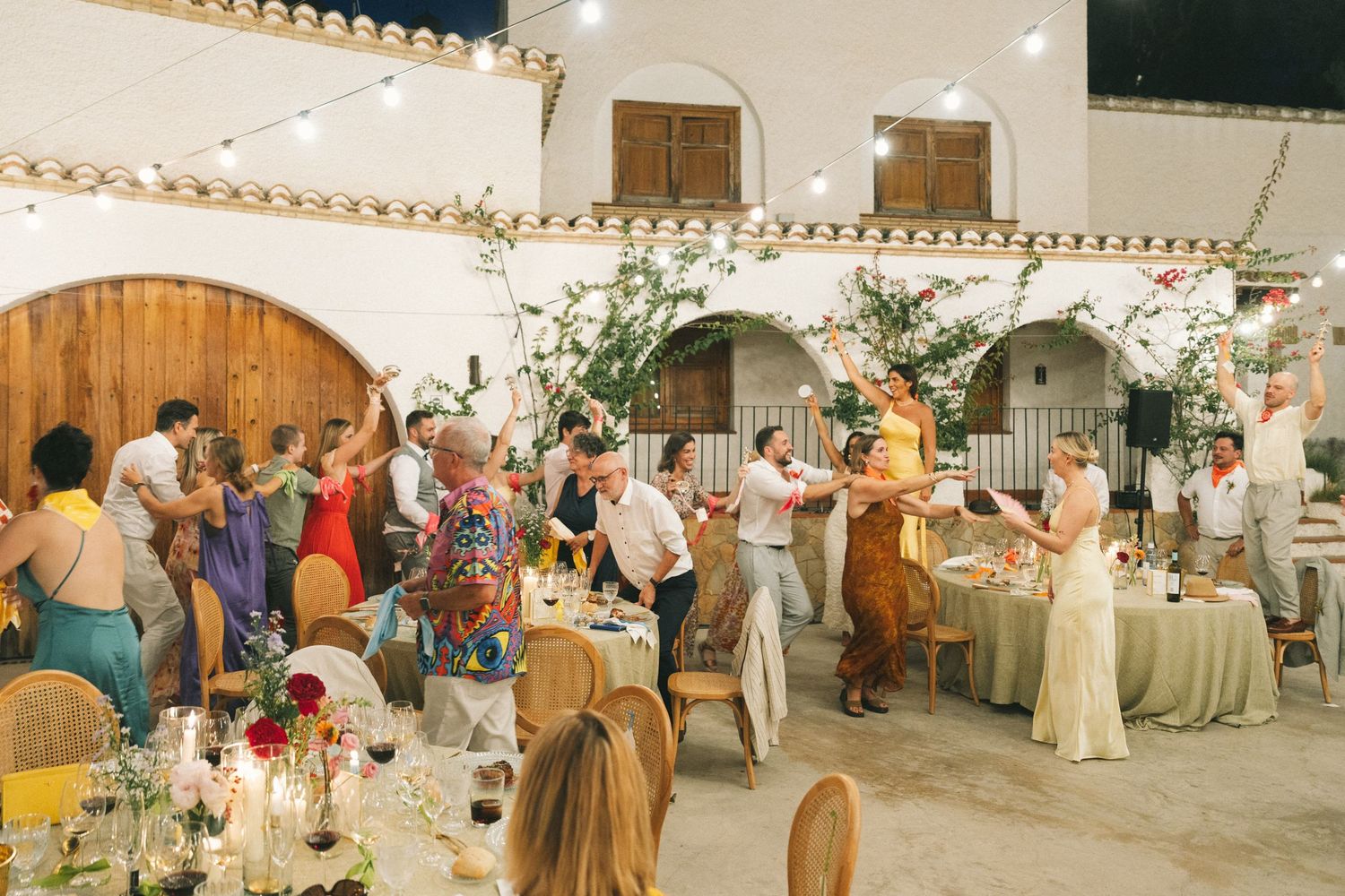 Wedding reception venue with guests mingling under string lights and white Spanish-style architecture.